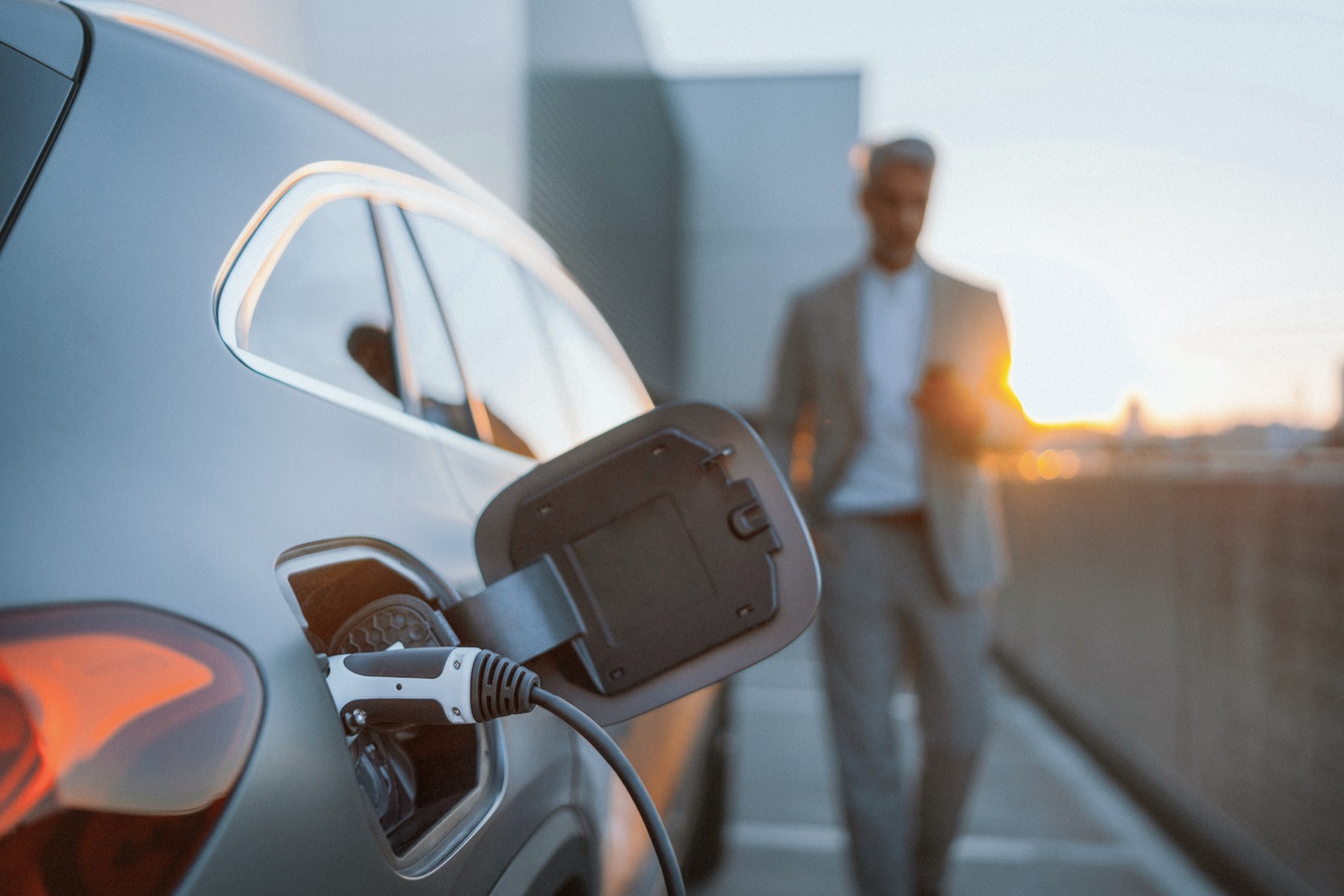 Mann lädt ein Elektroauto bei Sonnenuntergang